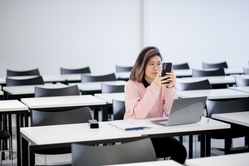 Kuvassa opiskelija istuu yksin luokkahuoneessa ja katsoo kännykkää.