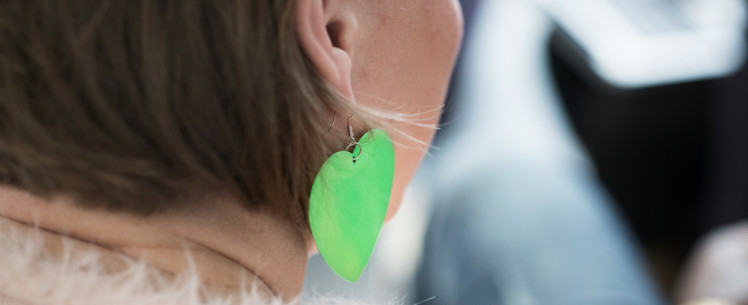 Vihreä sydänmallinen korvakoru naishenkilön korvassa, kuvituskuva.